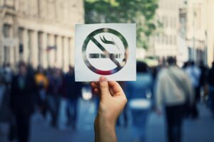 Hand holding a cutout "no smoking" symbol in front of a blurry crowd on a street