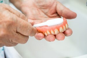 Hands holding a set of dentures and white toothbrush to clean them