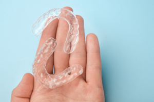 A hand on a blue background holding two Invisalign trays